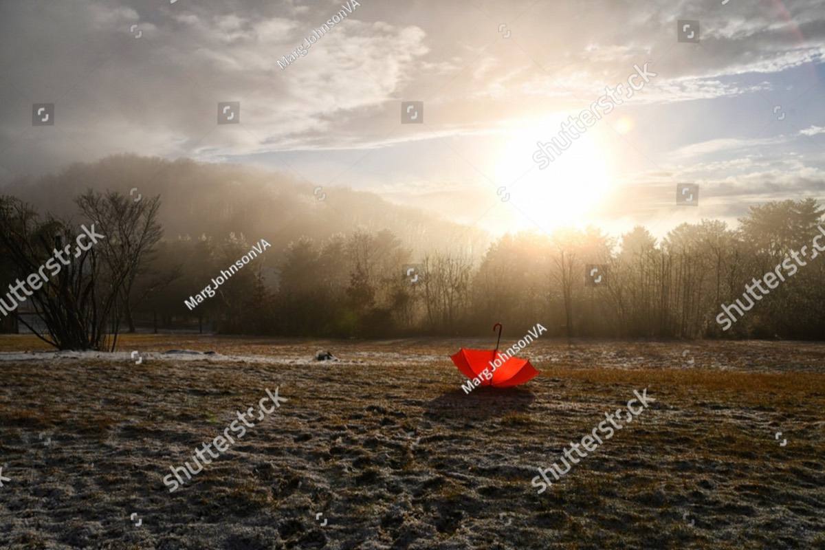 A red umbrella resting open on a field as sunbeams break through the mist