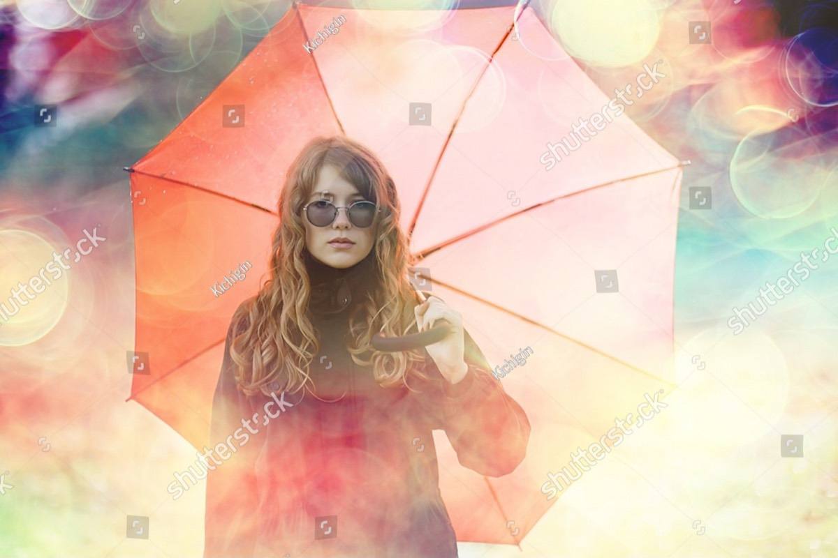 A woman standing beneath a coral umbrella in soft, warm light