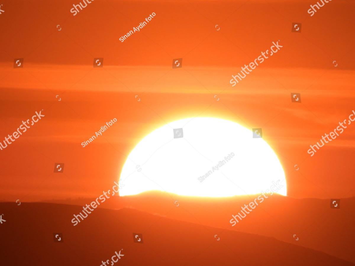 A large sun sitting low on the horizon in a deep orange sky